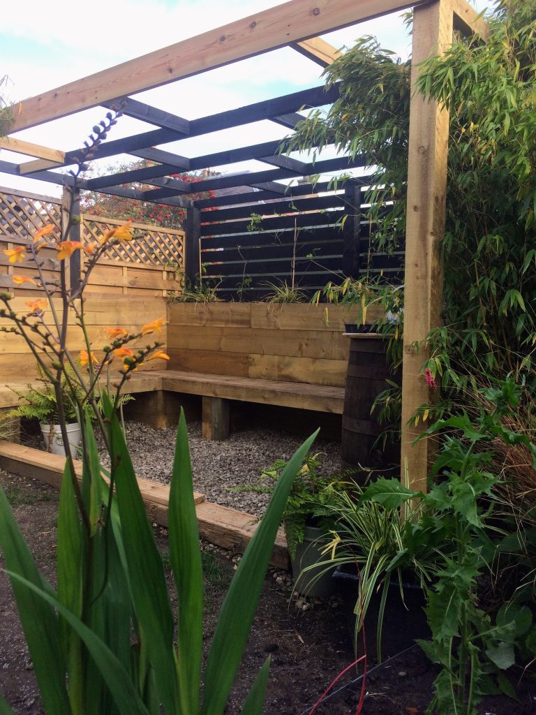Garden with a wooden pergola, built-in bench, and lush planting.